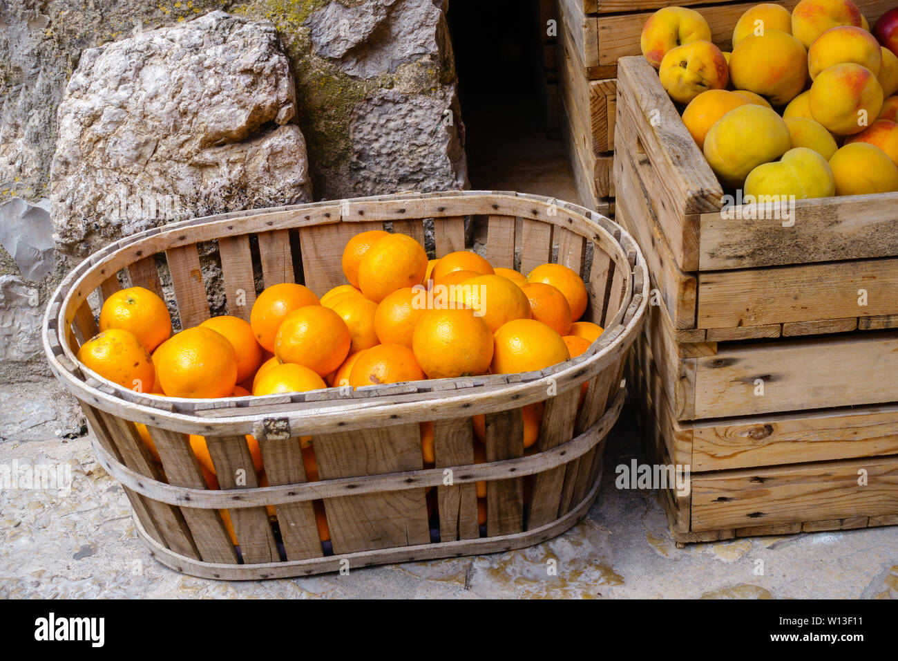 Ripe oranges and peaches in wooden box and basket at a food market - close-up on oranges, horizontal landscape format Stock Photo