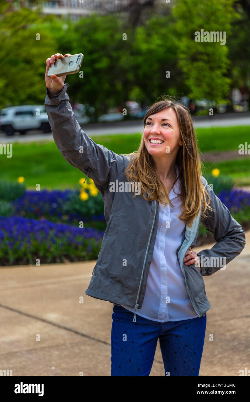 Young woman taking a selfie with her phone in a park.posomg Stock Photo