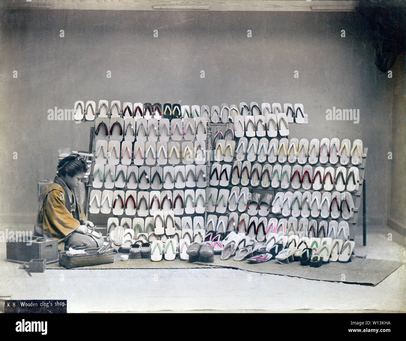 [ 1890s Japan - Geta Clog Store ] —   A studio photo of a woman selling geta, Japanese wooden shoe wear.   The roots of geta go back to the Yayoi era, but they became especially popular in the Edo Period (1600 - 1868). Geta craftsmen offered a wide variety of geta, depending on the fashion of the time.  19th century vintage albumen photograph. Stock Photo