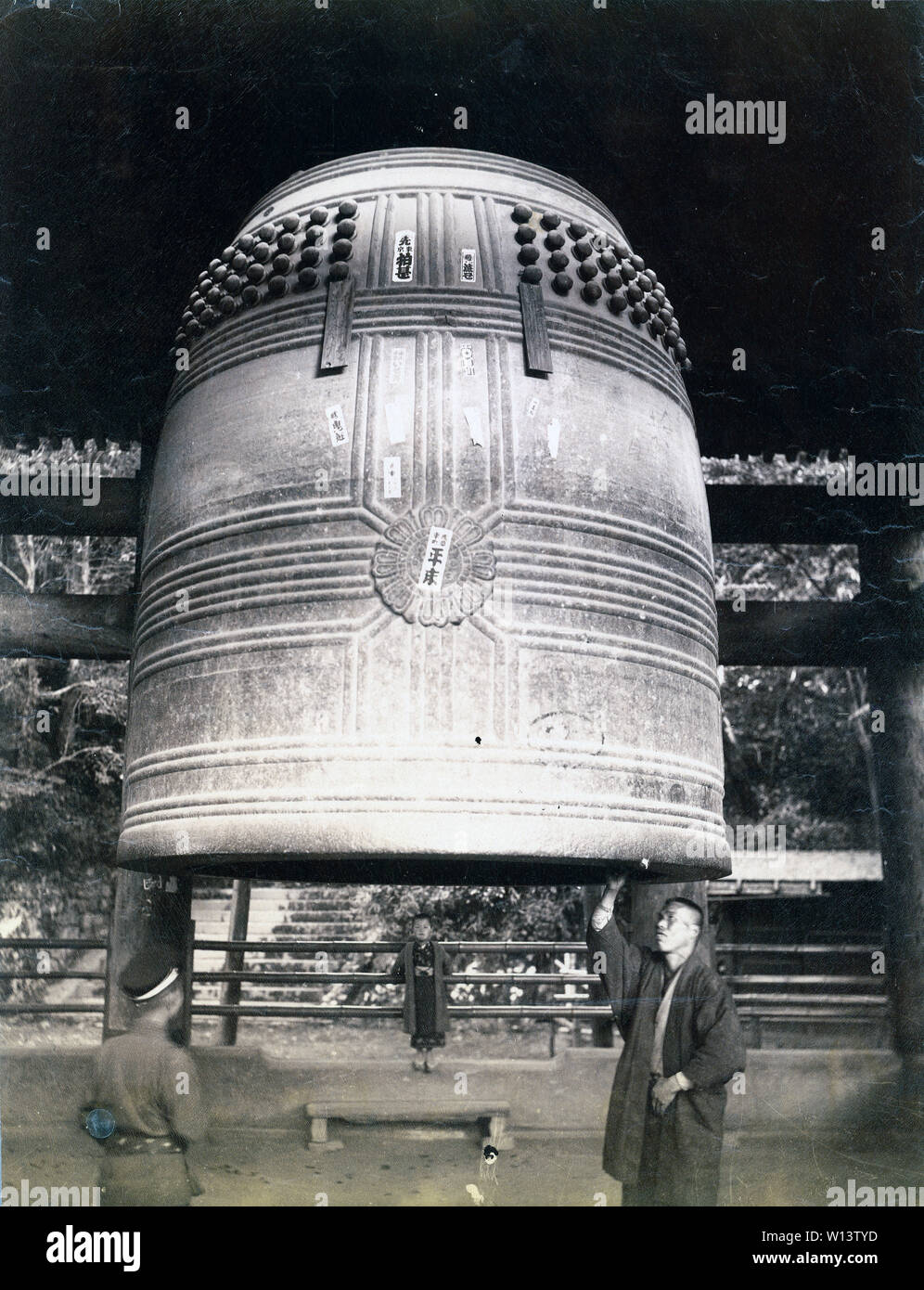 [ 1890s Japan - Large Temple Bell at Chion-in, Kyoto ] —   A man is stretching his arm to reach the bronze temple bell of Chion-in temple in Kyoto. The bell was cast in the early 17th century and was 4.5 meters high.  19th century vintage albumen photograph. Stock Photo