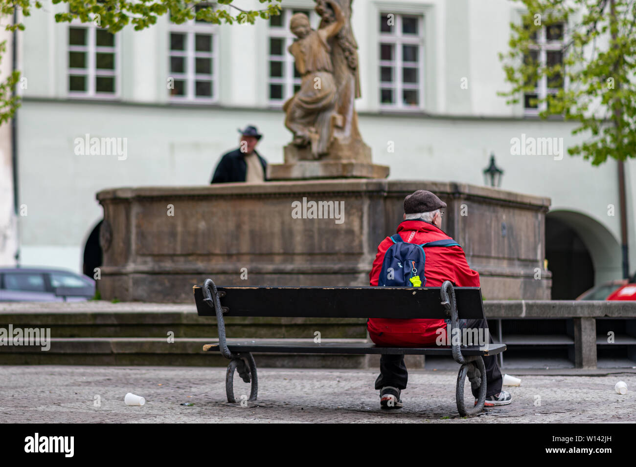 PRAGUE, CZECH REPUBLIC - 12TH APRIL 2019: A lone elderly male man sits on a bench in front of a statue in the middle of Prague Capital City Stock Photo