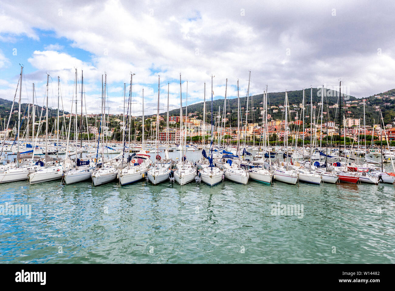 Sailboats neatly in a row in the harbour and houses on the hills, against cloudy sky in Lerici in Liguria, Italy Stock Photo