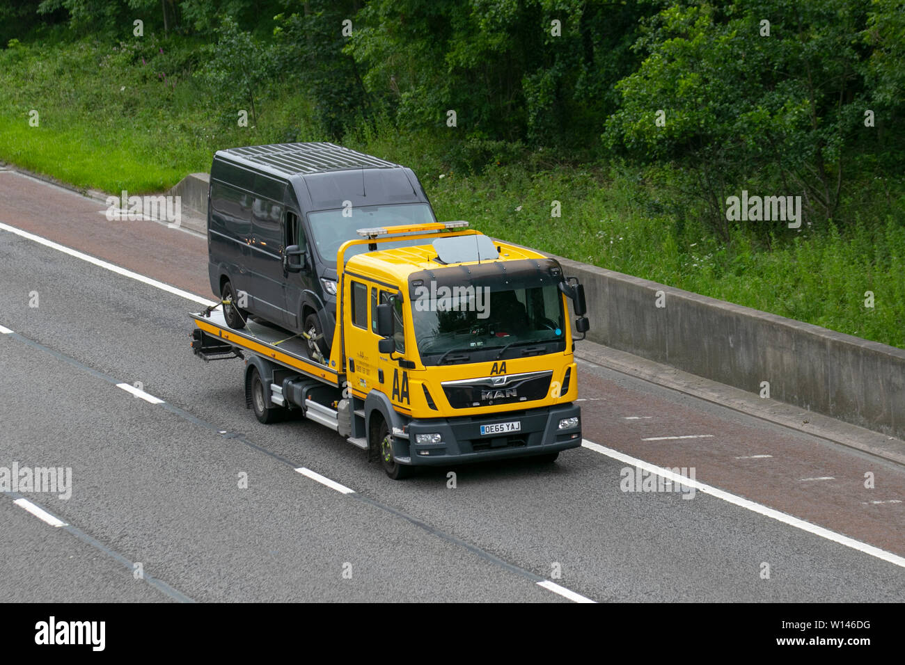 AA Van recovery truck carrying broken down van; Side view of rescue breakdown recovery lorry truck transporter transporting unmarked black van driving along  M6, Lancaster, UK; Vehicular traffic, transport, modern, north-bound on the 3 lane highway. Stock Photo