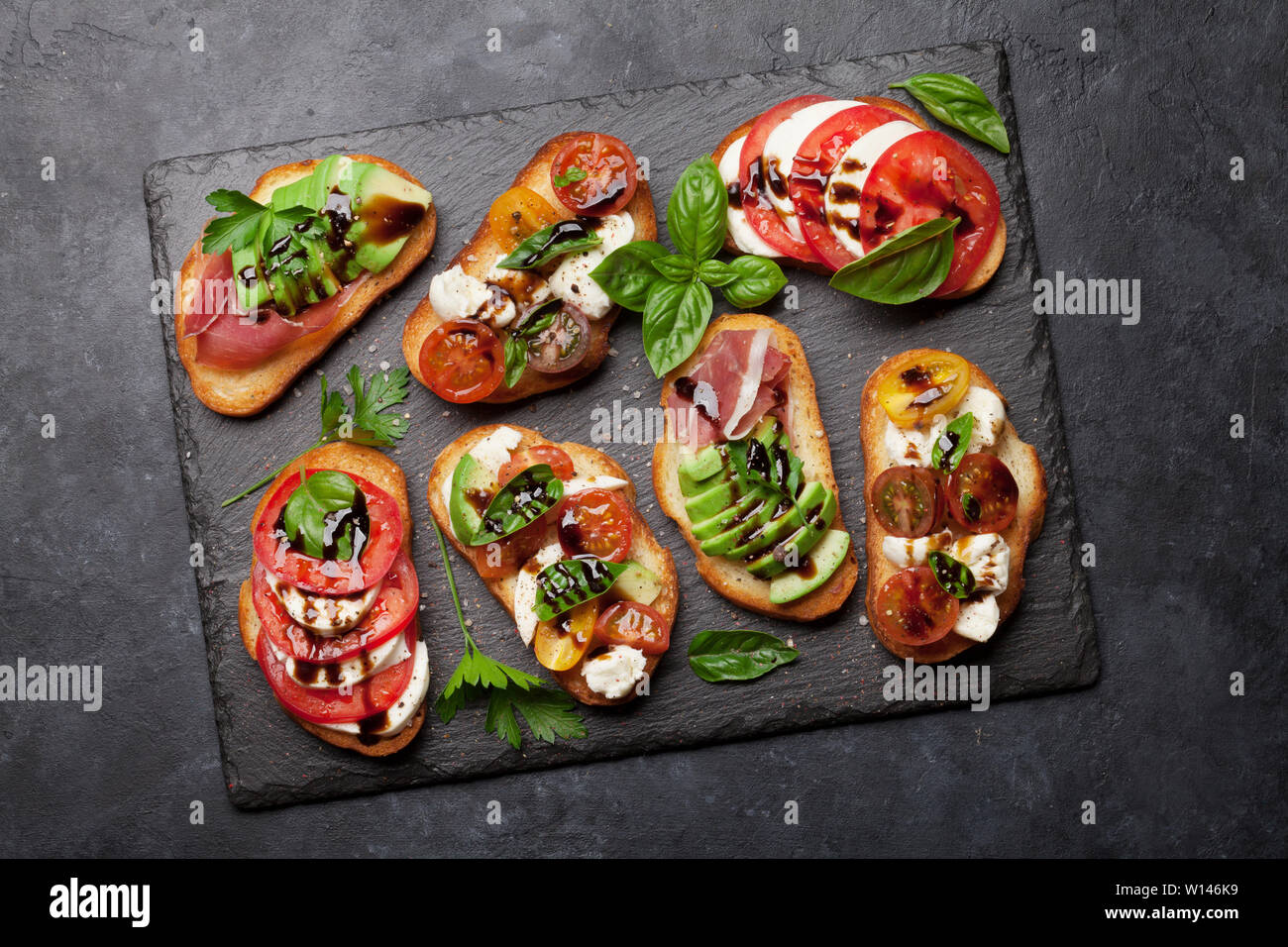 Traditional spanish tapas with tomatoes, mozzarella cheese, avocado and  prosciutto on black stone background. Flat lay. Top view Stock Photo - Alamy