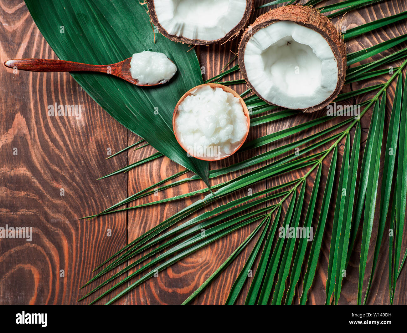 Top view of coconut MCT oil in bowl and in spoon and halved coco-nut on wooden table. Health Benefits of MCT Oil. MCT or medium-chain triglycerides, form of saturated fatty acid. Flat lay. Copy space Stock Photo
