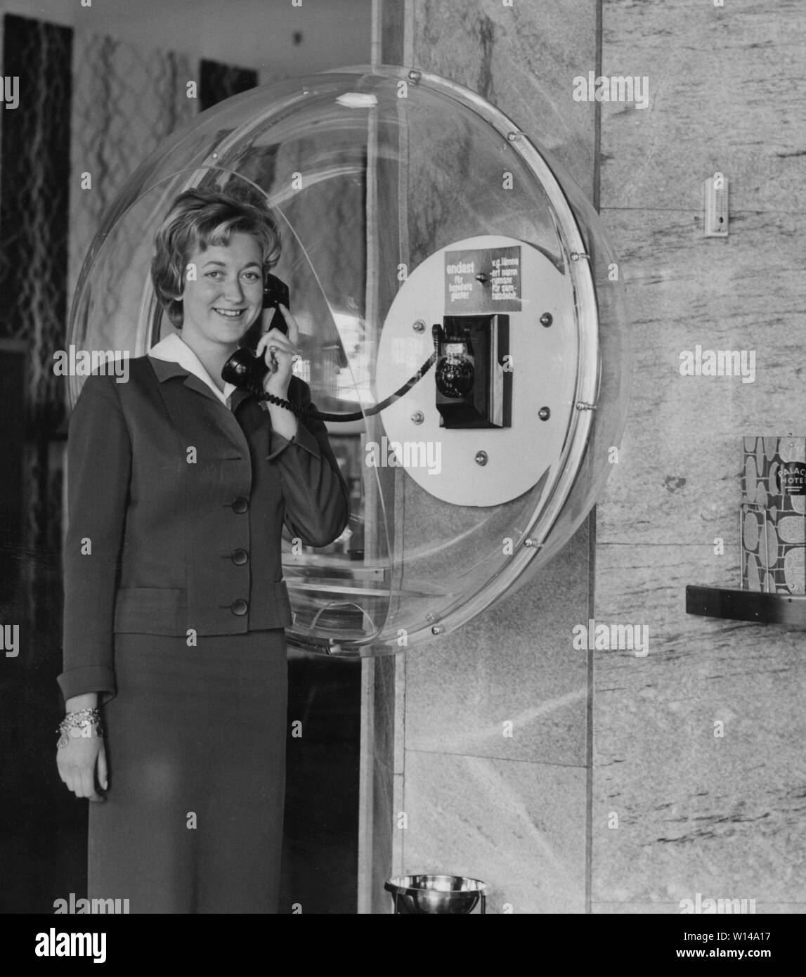 Phoning in the 1950s. An employee of a Palace hotel is showing the new courtesy phone installed in the lobby. Telephone in the 1950s. She is wearing a typical 50s dress and having a telephone conversation. The acrylic dome is a functional design where the person talking, is not being overheard by someone and also blocking the surrounding background noice. Sweden 1950s Stock Photo
