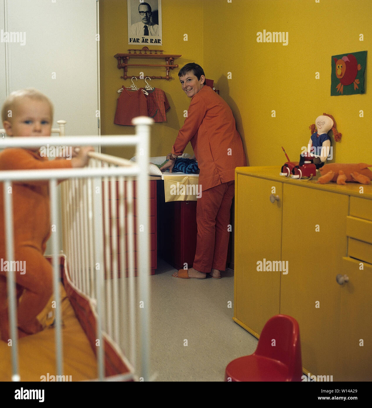 1960s mother. A young woman is cleaning and changing diapers on her baby that lies on a changing table. The clothes and colors are typical 1960s. Sweden 1964 Stock Photo