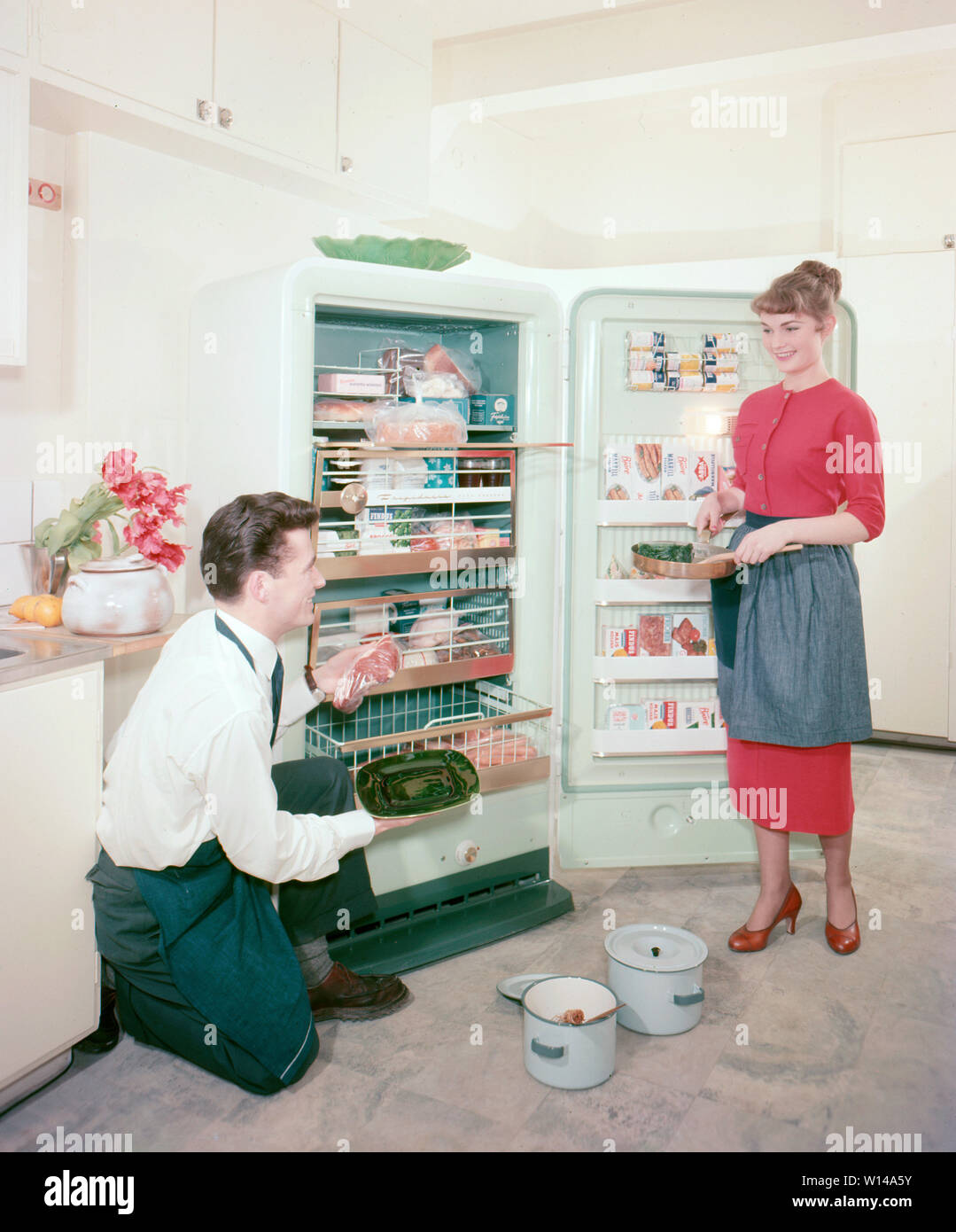In the kitchen 1950s. A young couple in their kitchen proudly showing their new Frigidaire freezer. ref BV66-4 Stock Photo