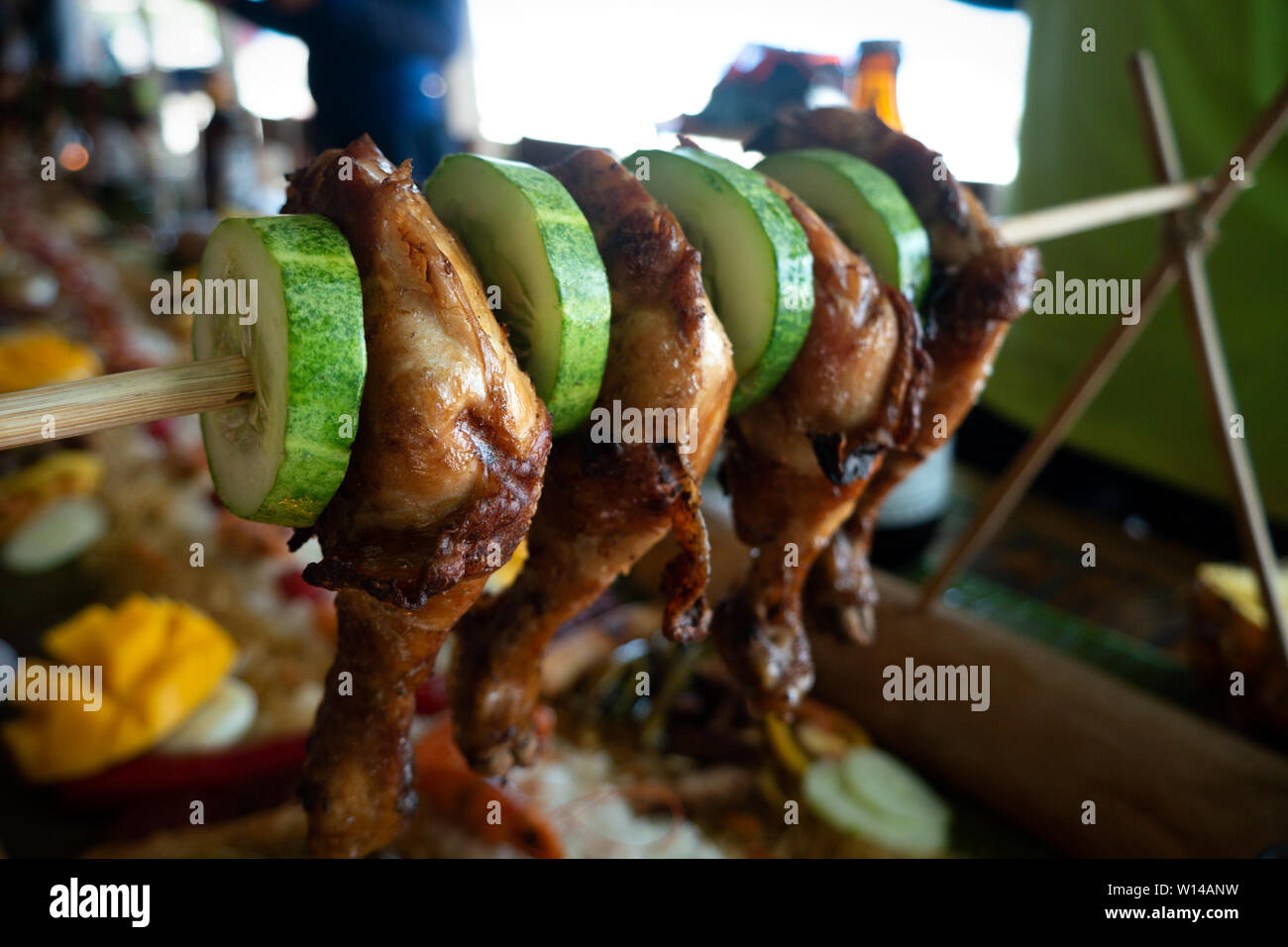 Filipino traditional authentic dish: philippine roasted chicken legs barbecue on a stick with cucumber Stock Photo