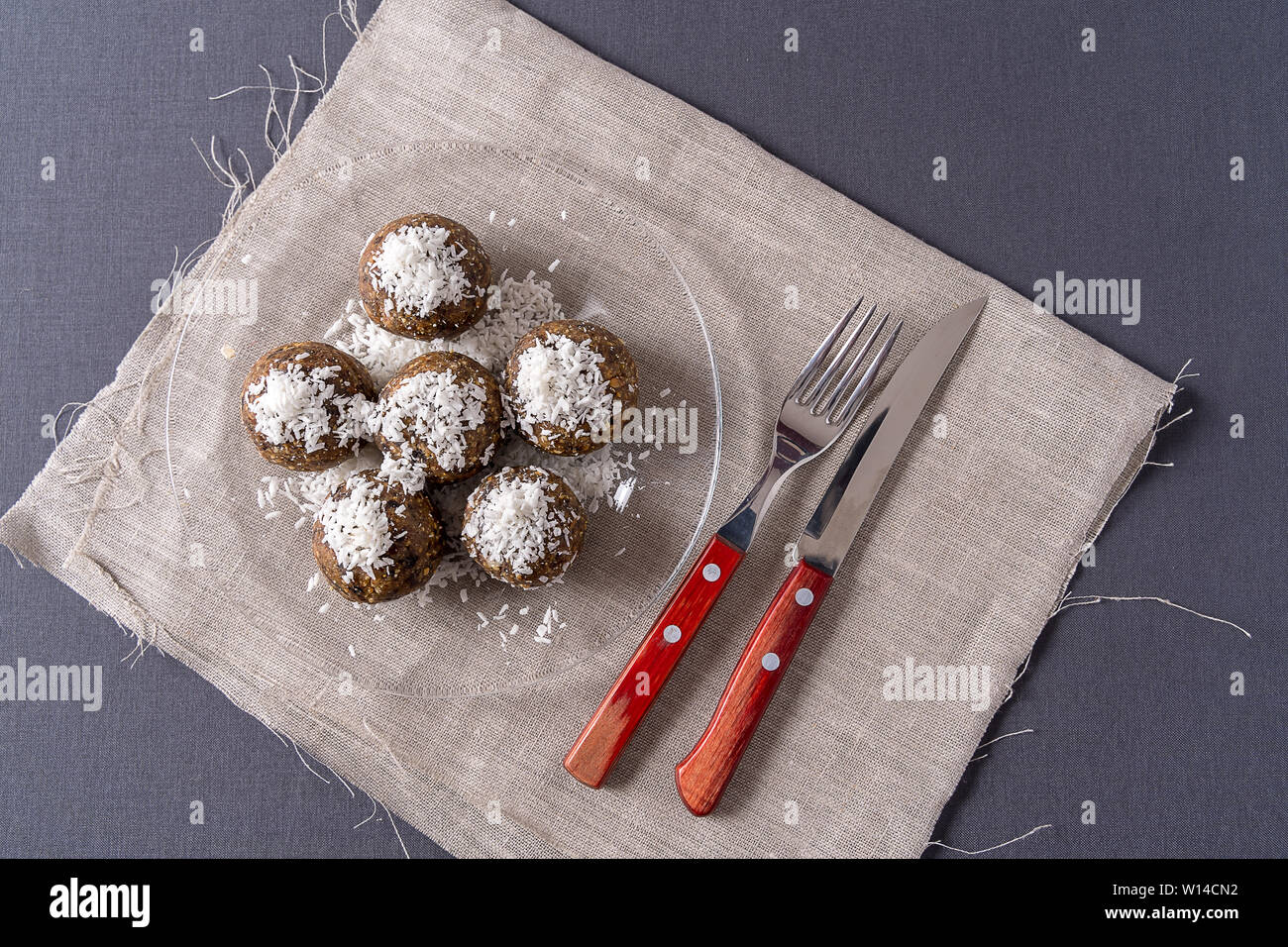 Healthy organic energy balls made with dates, prunes, raisins, peanut, with coconut shavings, in a glass plate on gray background, flat lay. Stock Photo