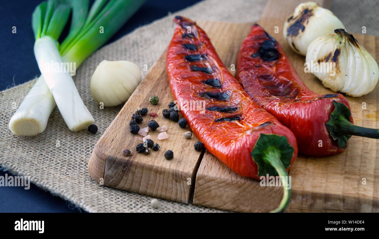 Roasted red bell pepper on wooden chopping board with condiments Stock ...
