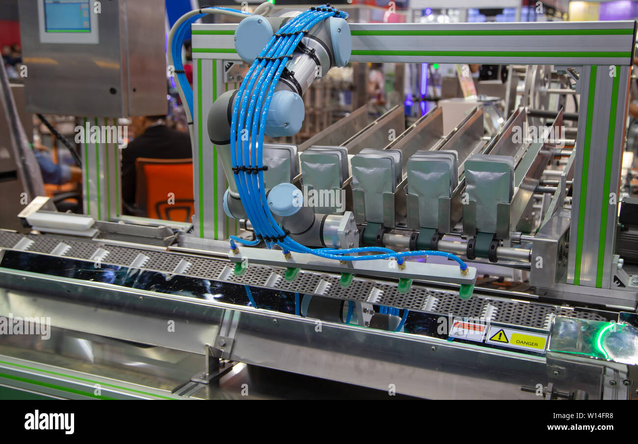 Automatic robotic arm loading aluminum pouch packaging to conveyor Stock Photo