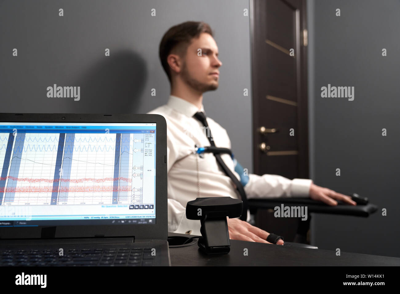 Selective focus of computer with diagrams for pulse indicating. Man sitting on chair and answering questions during lie test at background. Modern dev Stock Photo
