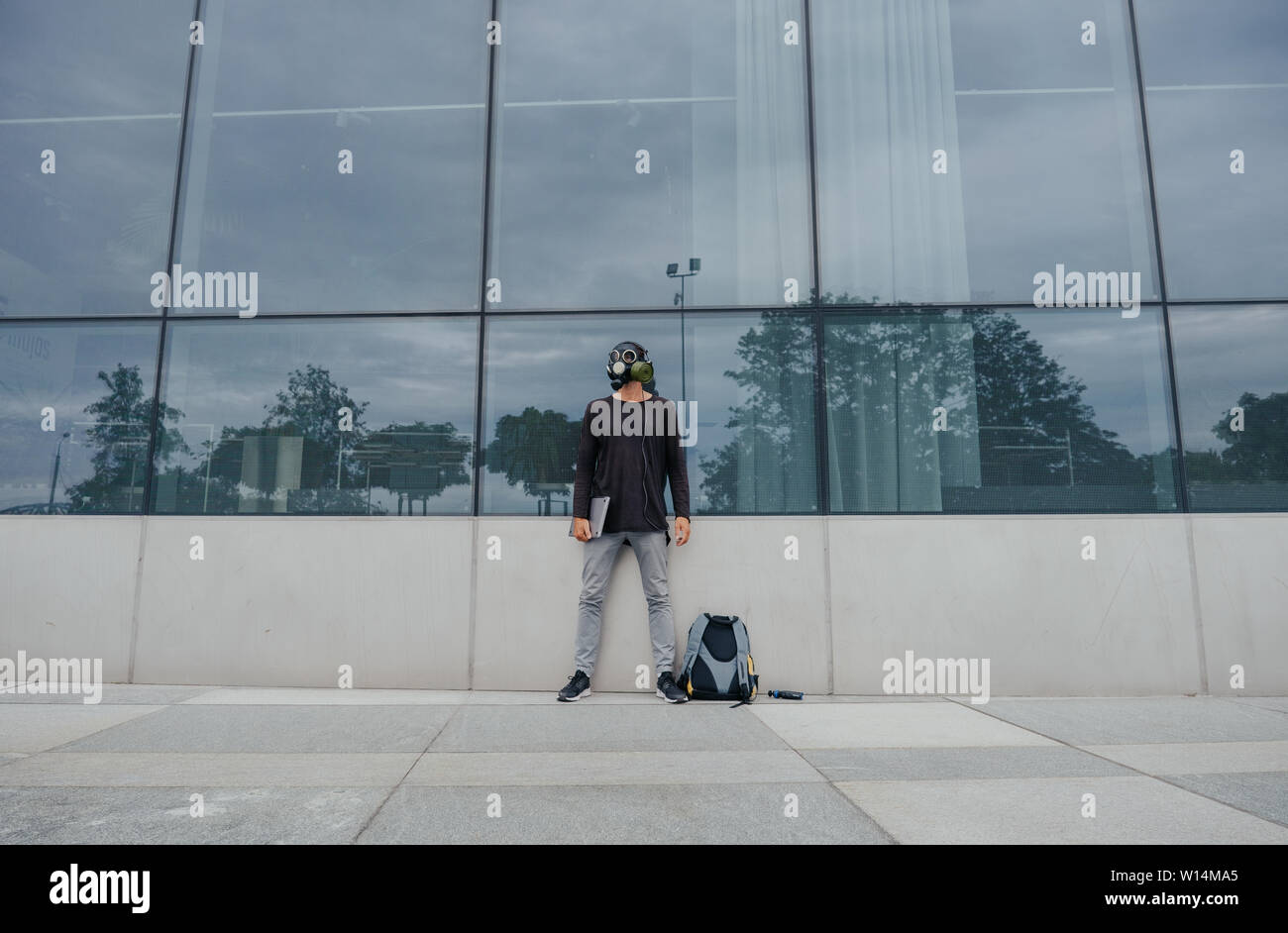 A city man in a gas mask works and listens to music against the background of a building and trees in a vacuum without people Stock Photo