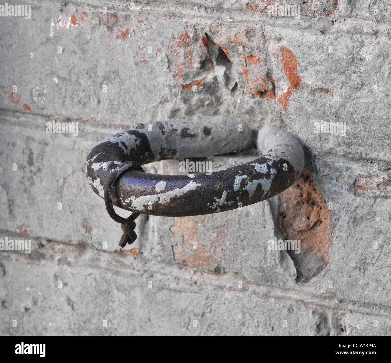 Ancient horse hitching post ring on a heritage wall of red bricks roughly covered with gray plaster Stock Photo
