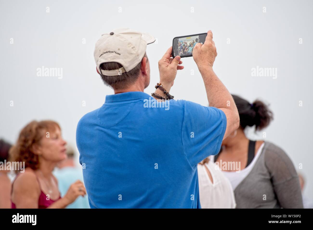 A man holds up his smart phone to take a selfie with the people that are standing behind him. Stock Photo