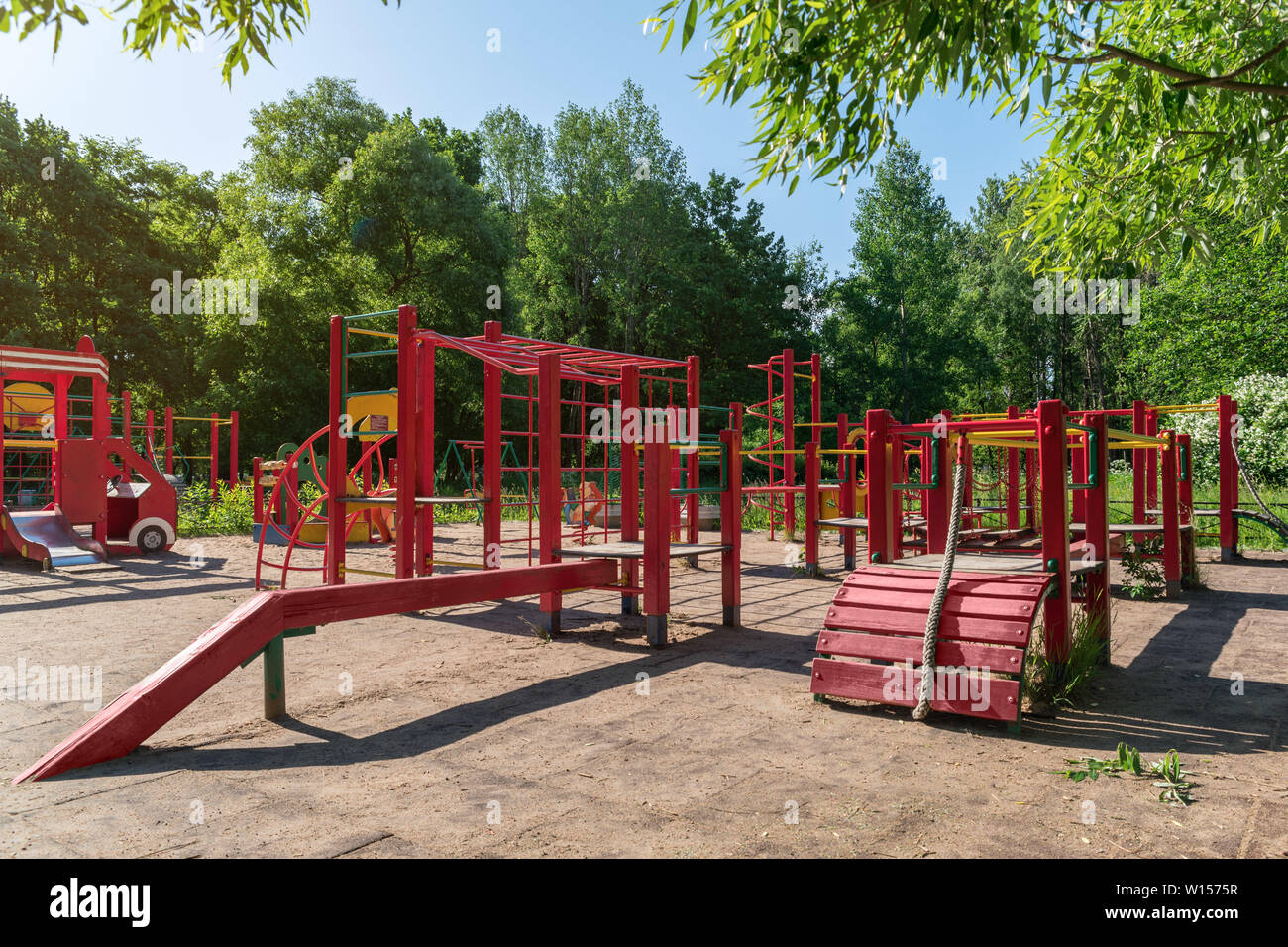 Children playground on yard activities in public park surrounded by green trees at sunlight morning. Children run, slide, swing,seesaw on modern playg Stock Photo