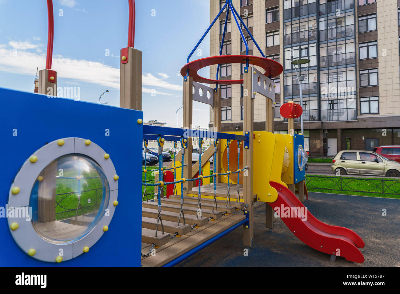 Children playground on yard activities in public park surrounded by green trees at sunlight morning. Children run, slide, swing,seesaw on modern playg Stock Photo