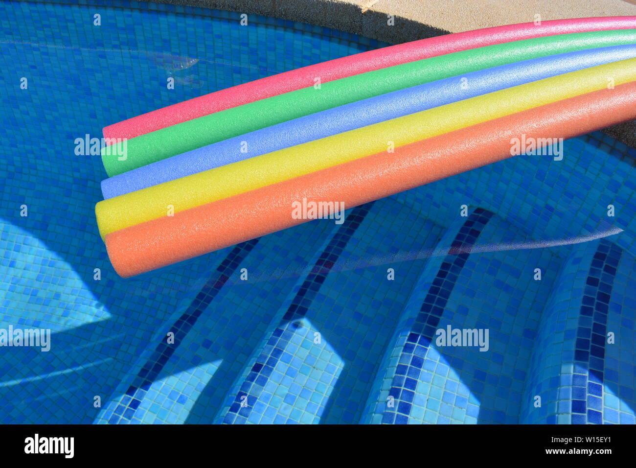 Brightly coloured pool noodles and swimming pool, with copy space. Fun, colorful, summer vibes