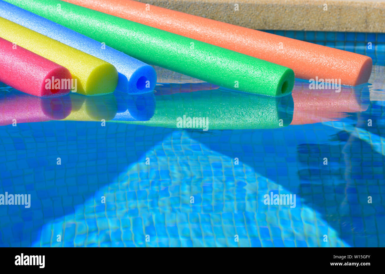 Brightly coloured pool noodles and swimming pool, with copy space. Fun