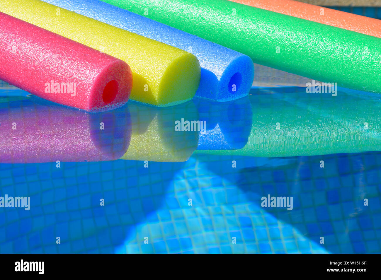 Brightly coloured pool noodles and swimming pool, with copy space. Fun