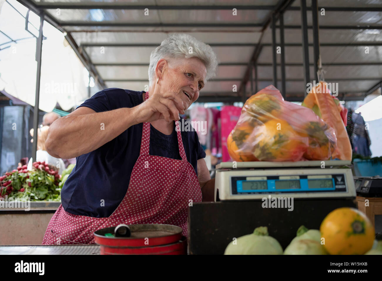 Belgrade, Serbia, June 28th 2019: Woman measuring zucchinis on a scale at the Zemun Green Market Stock Photo
