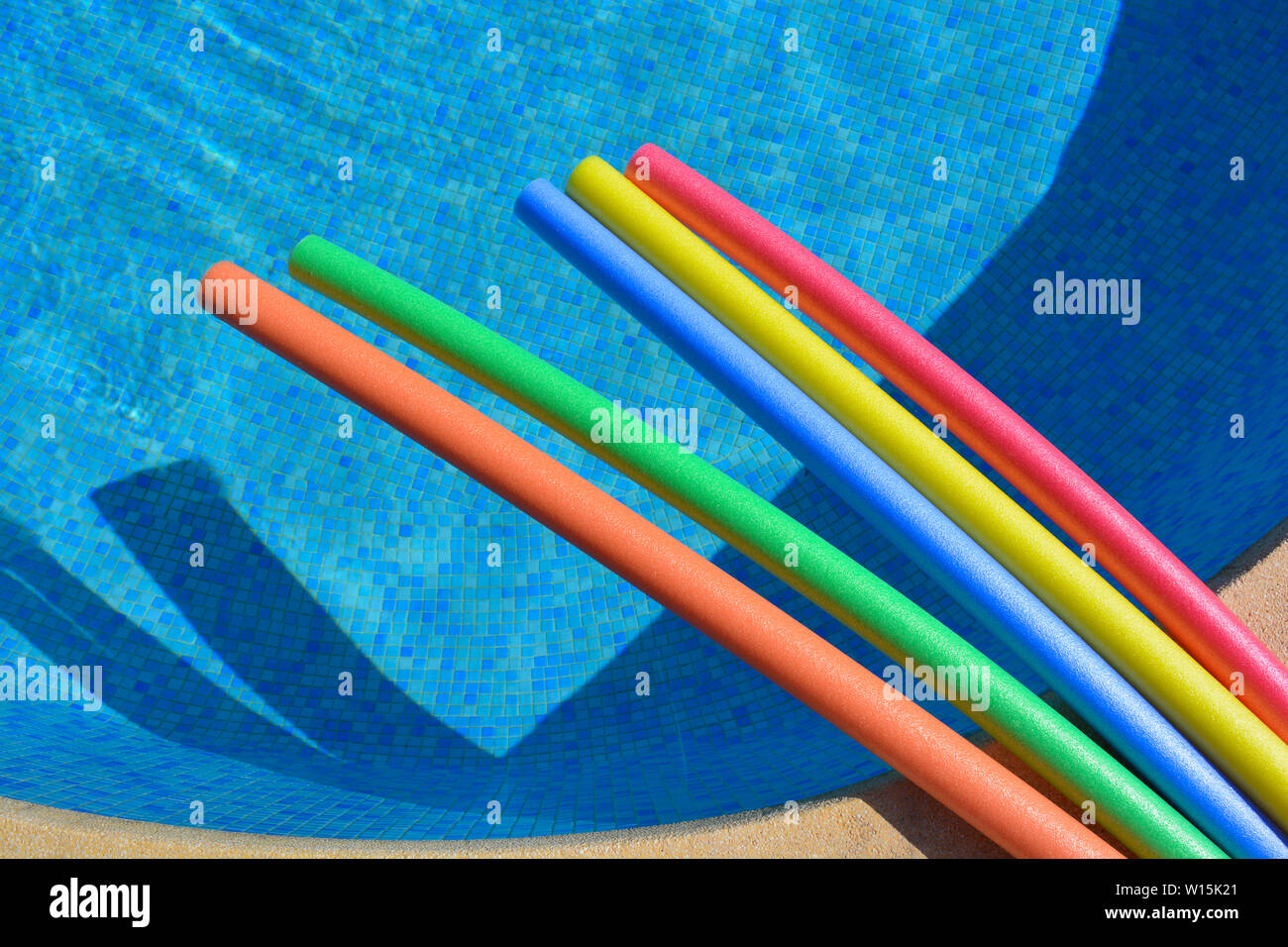 Brightly coloured pool noodles and swimming pool, with copy space. Fun