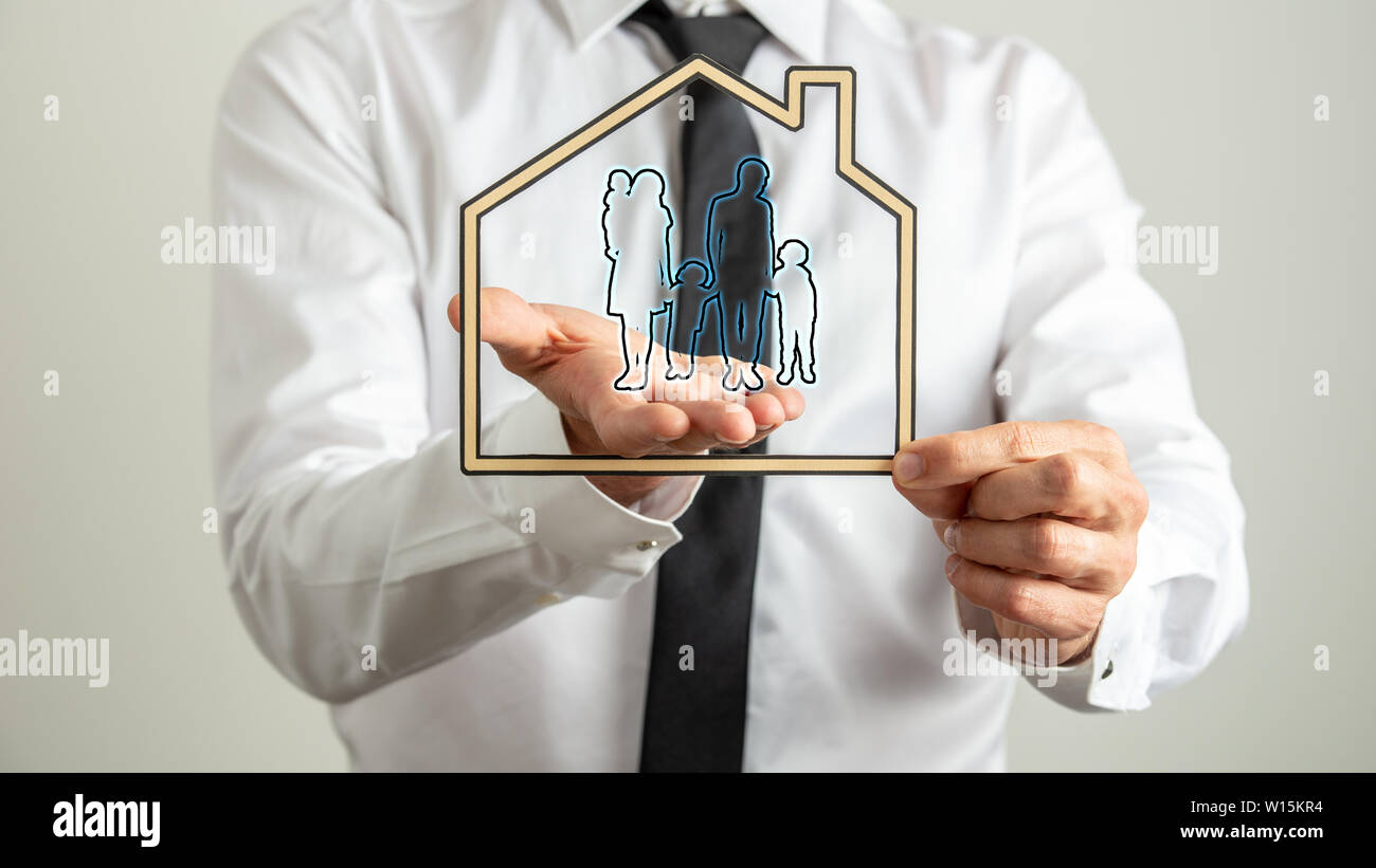 Businessman holding a paper cut house around a shape of a family in a conceptual image of insurance and safety. Stock Photo