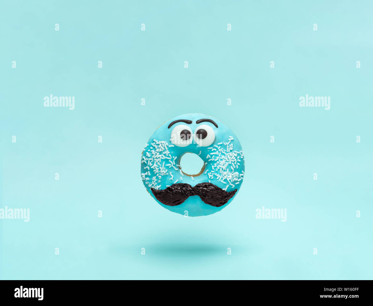 Blue glazed donut with mustache. Flying blue doughnut with funny face with mustache over blue background. Copy space for text. Masculinity or father day concept. Stock Photo