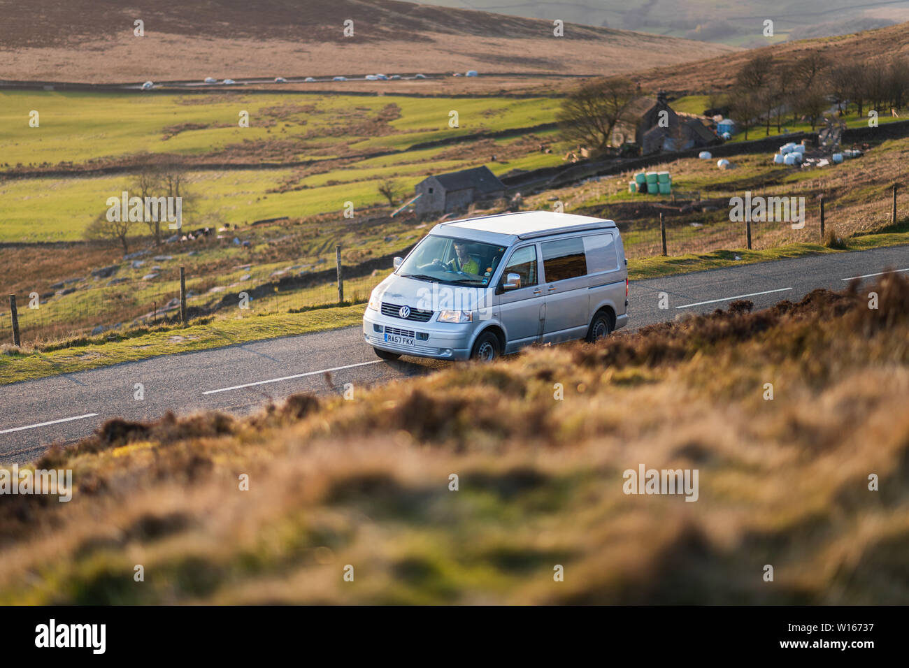 DERBYSHIRE, UK - 31ST MARCH 2019: A silver van drives through the Peak District during a low sunset Stock Photo