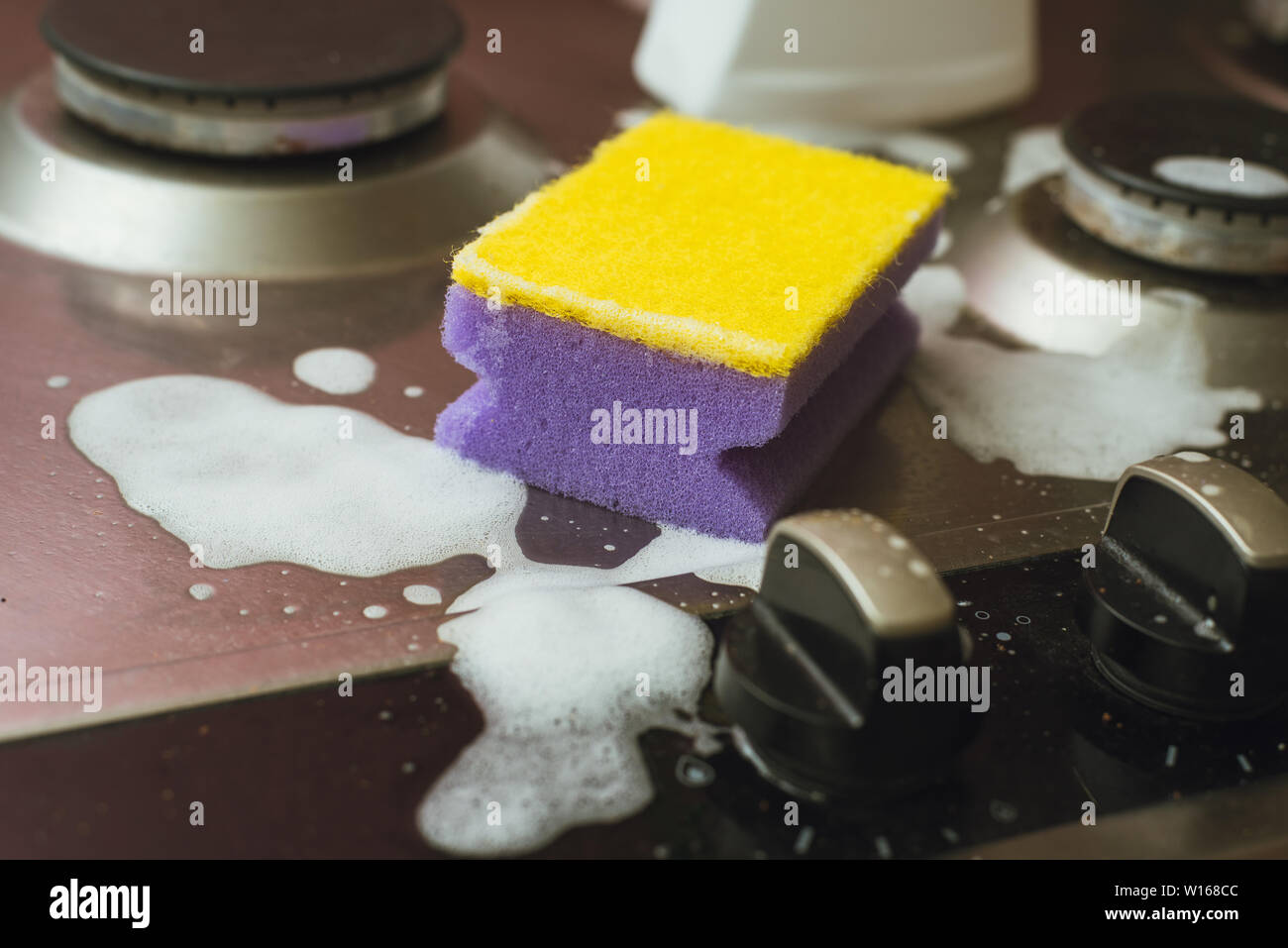 Violet yellow sponge with a metal gas stove. Cleaning the dirt with a