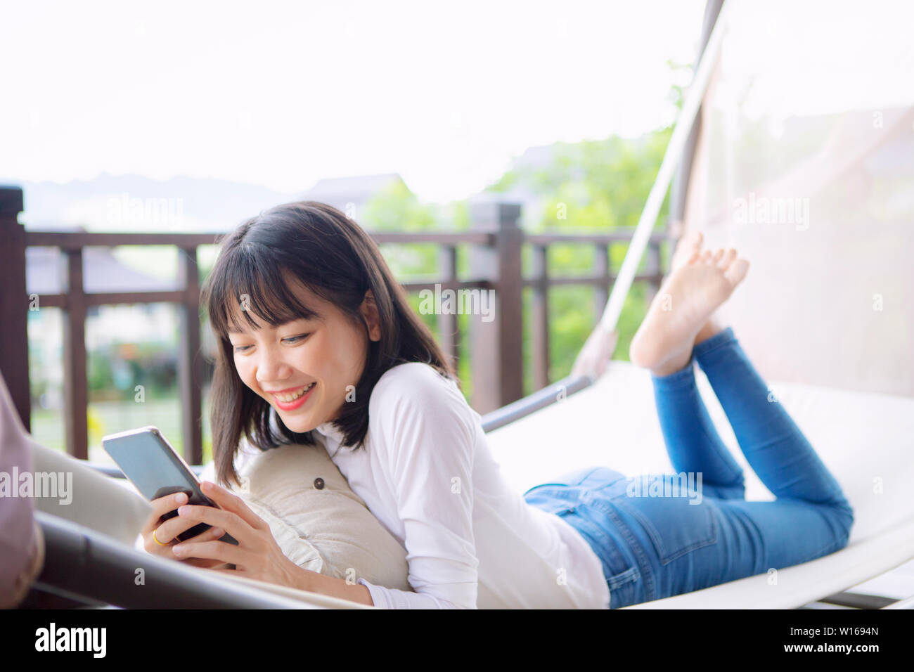asian younger woman toothy smiling with happiness holding smart phone in hand ,relaxing lifestyle Stock Photo