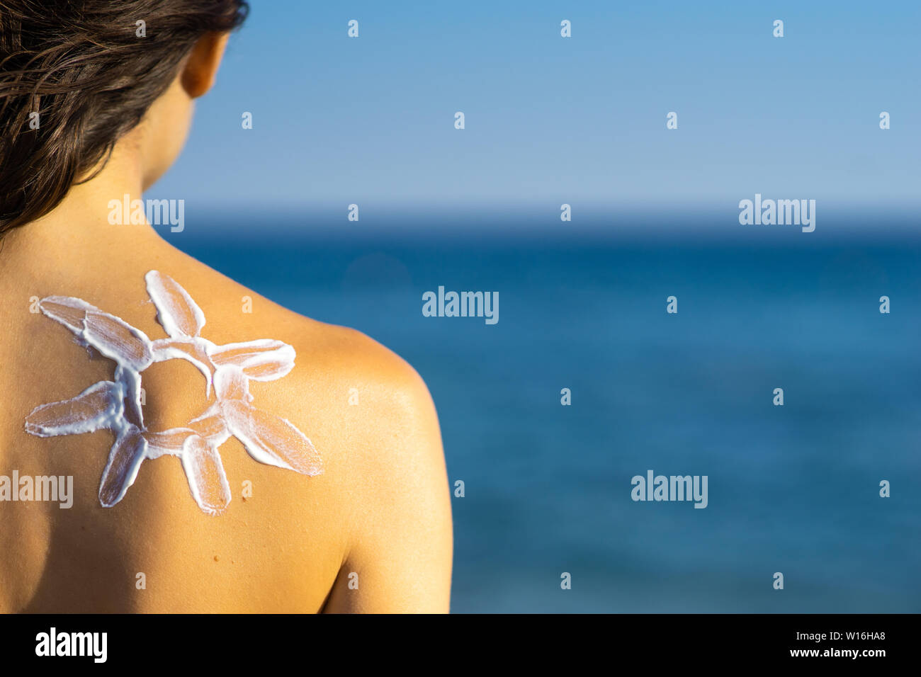 skin protection - young woman with sun-shaped sun cream on her back at the sea. view from behind Stock Photo