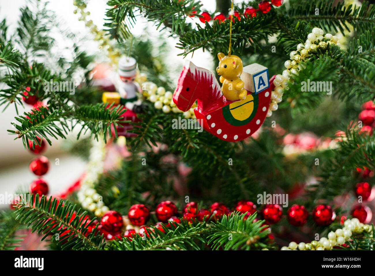 Close up of christmas ornament of red rocking horse with teddy bear and alphabet block hangs on branch of Christmas tree with red and white beaded gar Stock Photo
