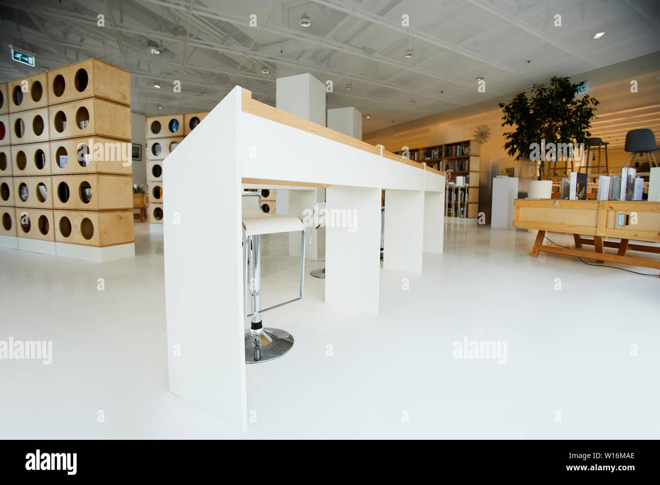 White angled tables and modern high chairs placed in center of bookstore room, creative bookcases in background Stock Photo