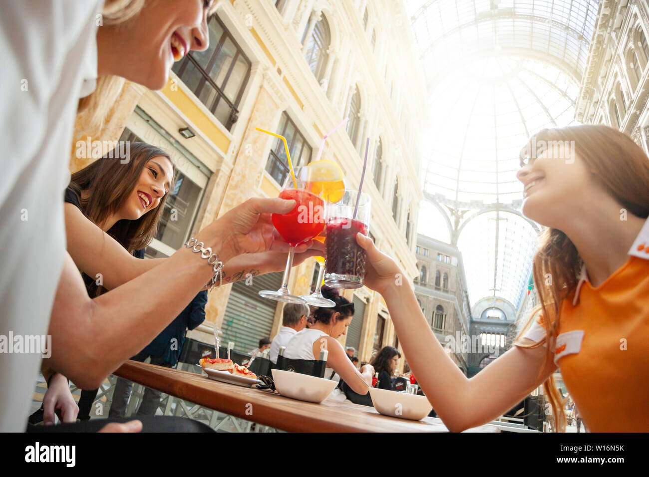 Friends do cheers with drinks in the gallery Umberto Primo in Naples. Stock Photo