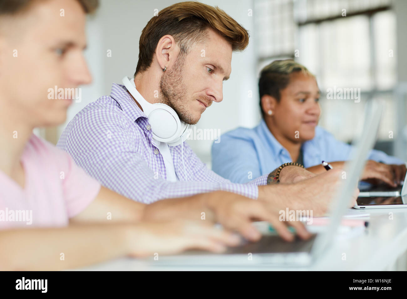 Serious concentrated hipster guy with stubble sitting at table and making notes in notepad while analyzing information Stock Photo