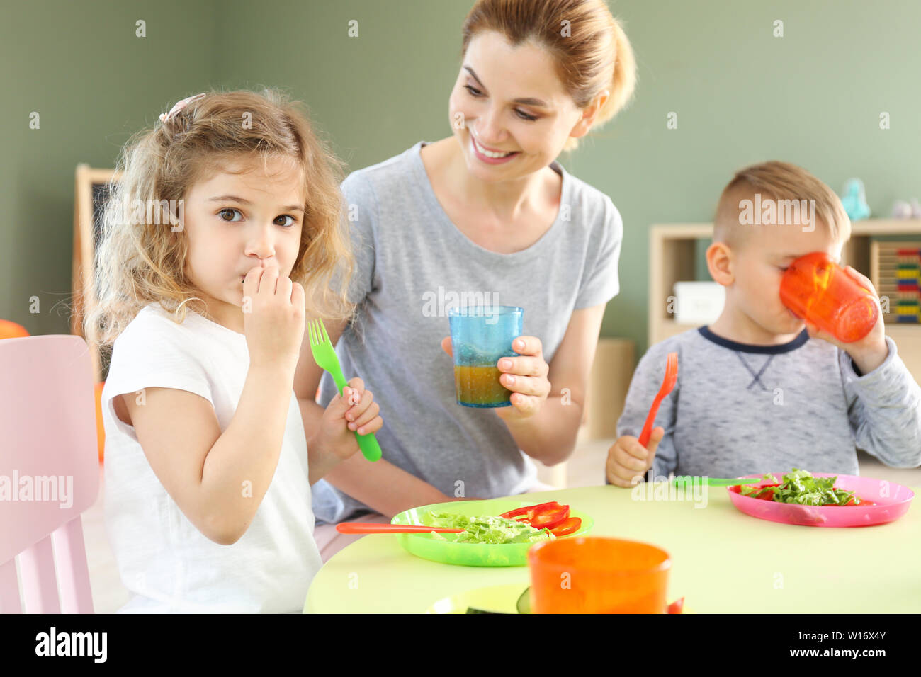 Nursery teacher with cute little children during lunch in kindergarten Stock Photo
