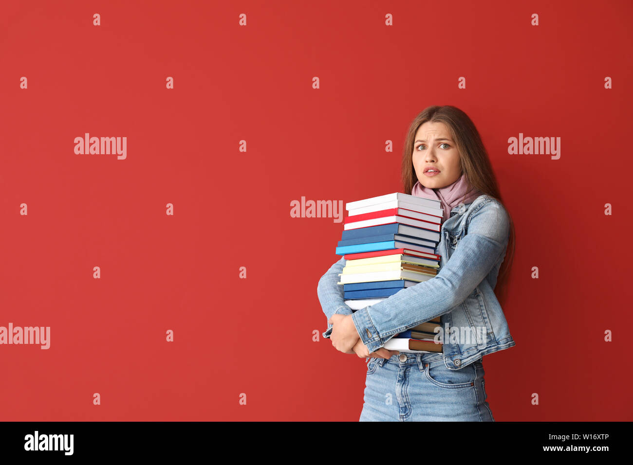 Stressed young woman with books on color background Stock Photo