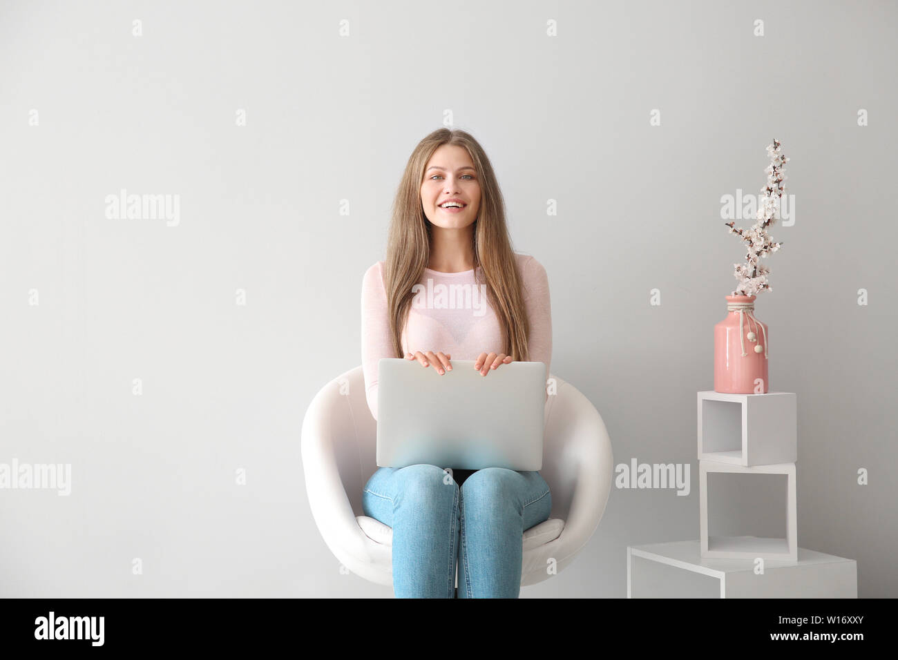 Beautiful young woman with laptop sitting on chair indoors Stock Photo ...