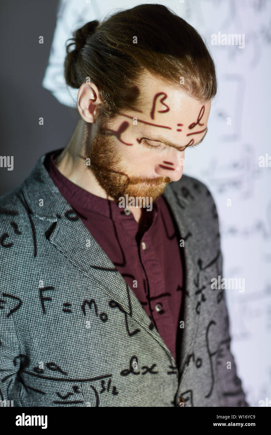 Serious pensive young bearded man in jacket looking down while giving conference presentation on math Stock Photo