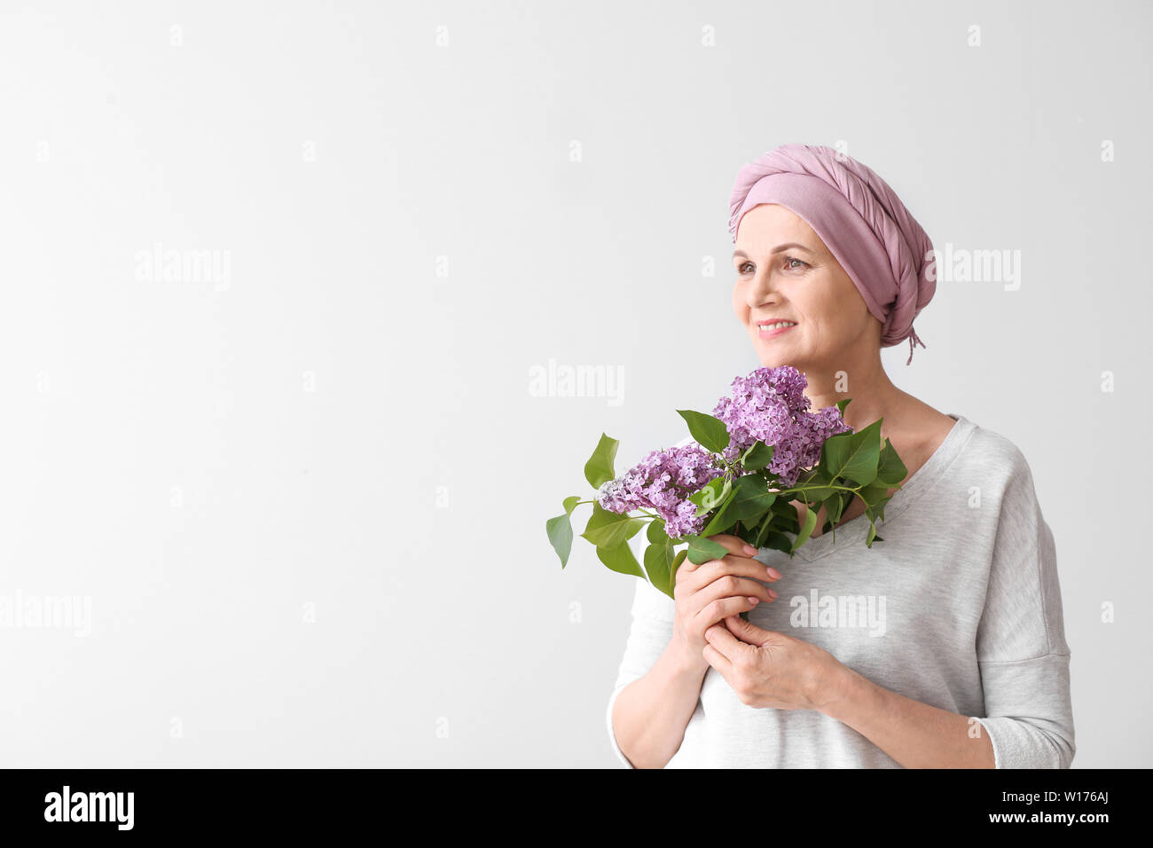 Mature woman after chemotherapy with bouquet of flowers on light