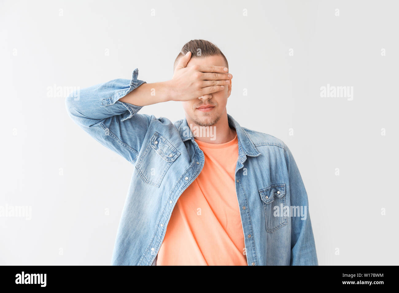 Young man covering his eyes on grey background Stock Photo - Alamy