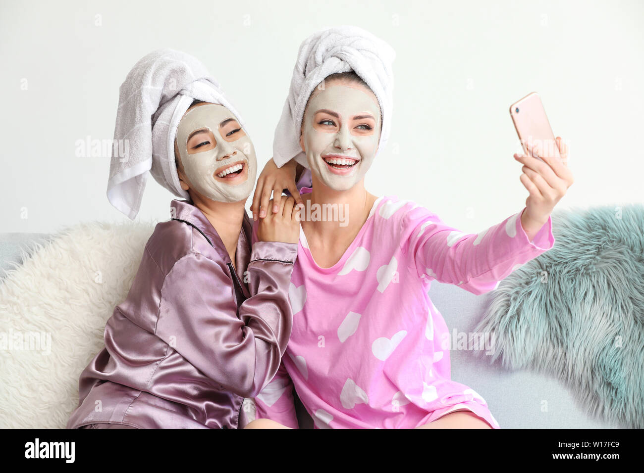 Beautiful young women with facial masks taking selfie at home Stock