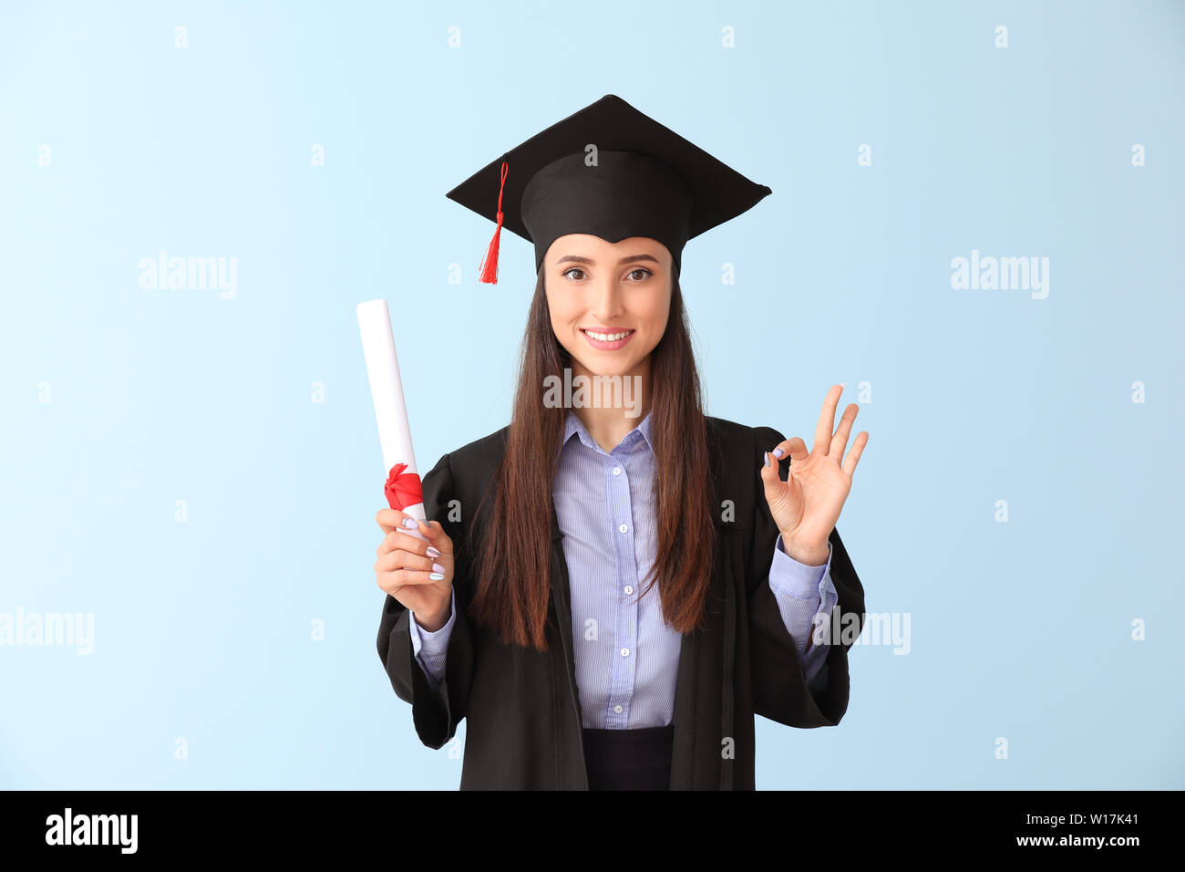 Female graduate with diploma showing OK on color background Stock Photo ...