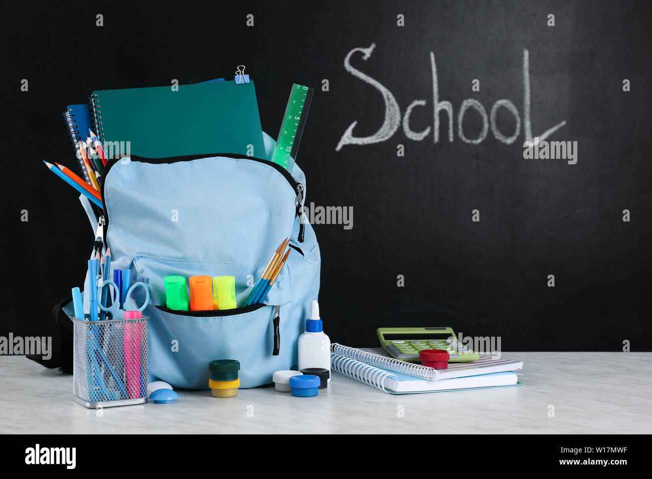 School backpack with stationery on table in classroom Stock Photo