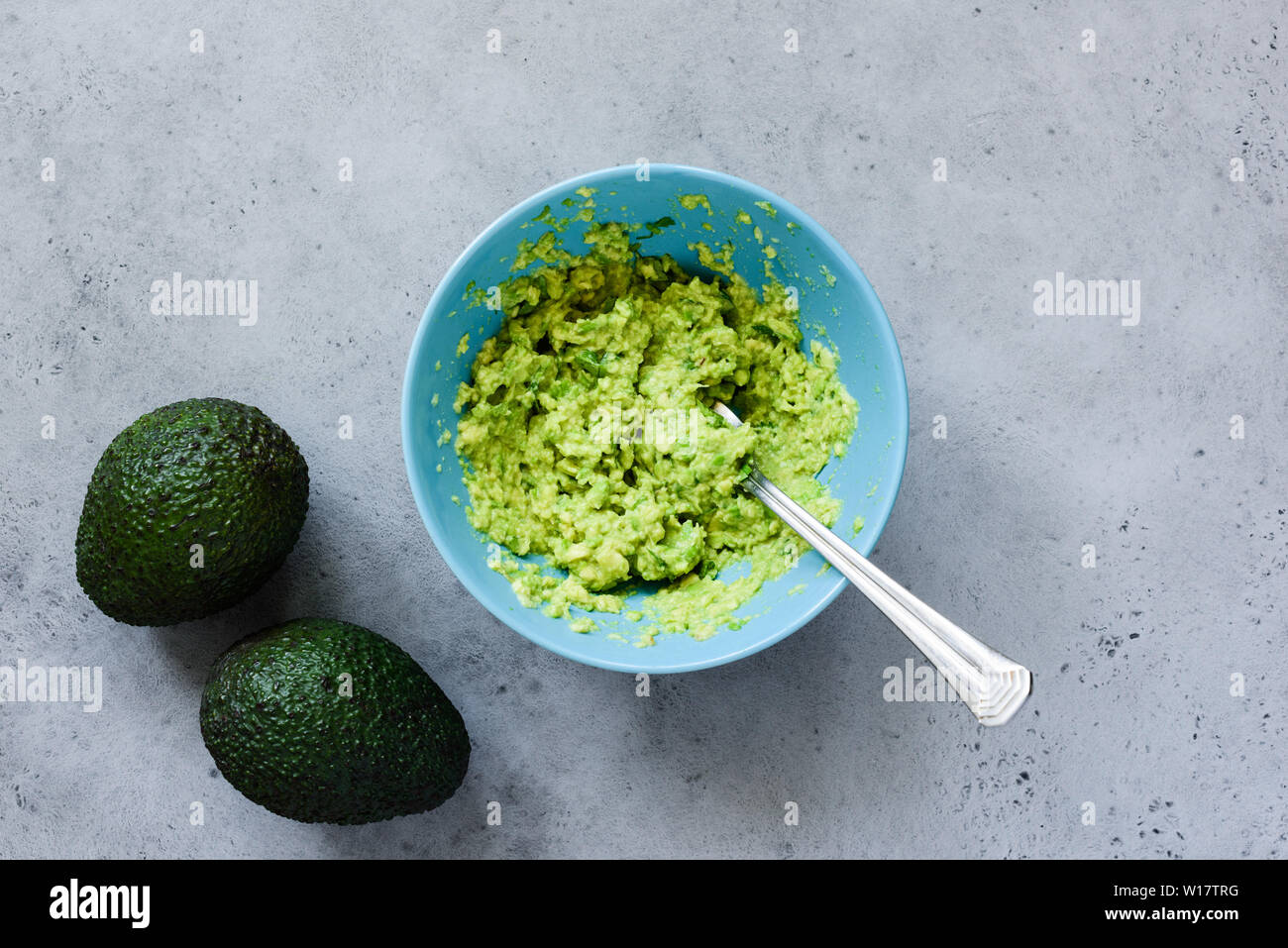 Mashed avocado in bowl on grey concrete background. Table top view. Cooking healthy vegan or vegetarian sauce or dip Stock Photo