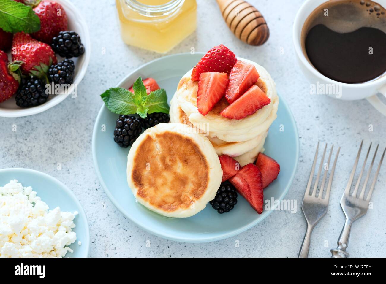 Cottage syrniki with strawberries, honey on blue plate and cup of black coffee on background. Healthy tasty breakfast Stock Photo