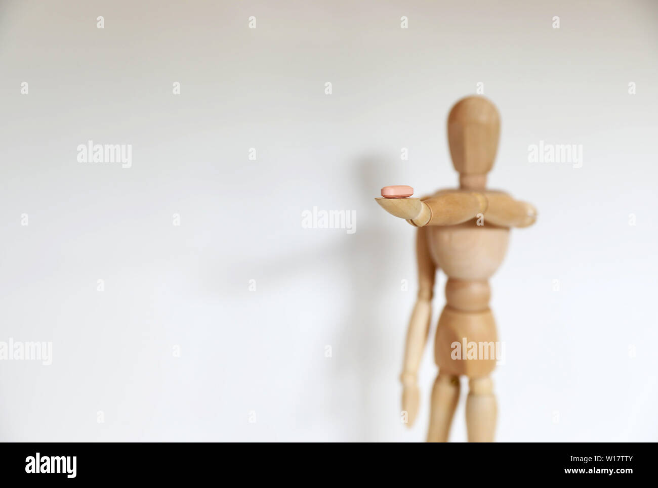 Single solo individual wooden mannequin figure offering dealing a pill drug to the viewer. Personal choice decision. Self harm damage and consequence Stock Photo