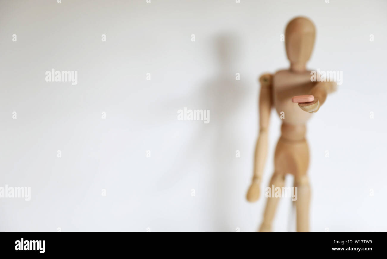 Single solo individual wooden mannequin figure offering dealing a pill drug to the viewer. Personal choice decision. Self harm damage and consequence Stock Photo